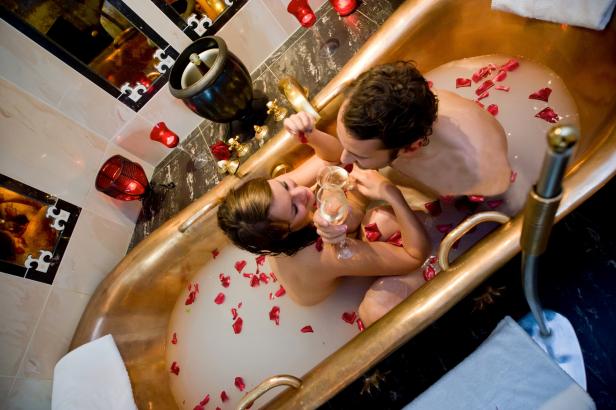 Ein Paar entspannt mit Champagner und Rosenblättern in einer goldenen Badewanne.