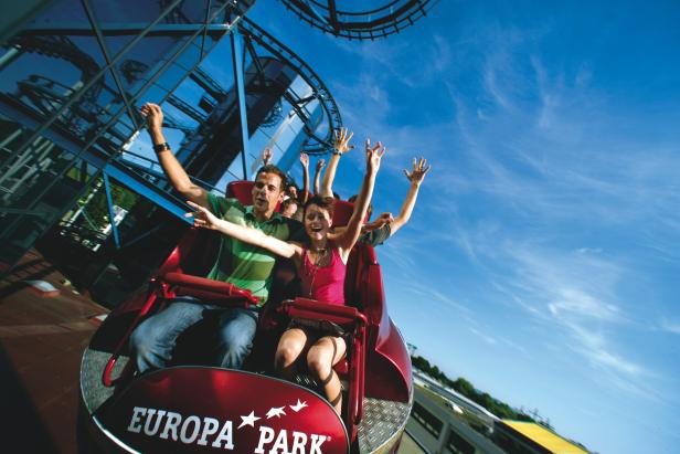 Menschen fahren mit erhobenen Armen in einer Achterbahn im Europa-Park.