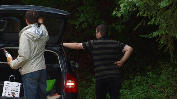 Zwei Männer packen einen Kofferraum voller Einkäufe in der Natur aus.