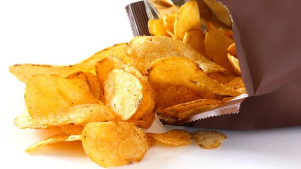 Kartoffelchips fallen aus einer geöffneten Tüte.