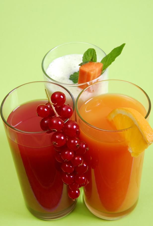 Drei Gläser mit verschiedenen Säften und Fruchtdekoration auf einem grünen Hintergrund.