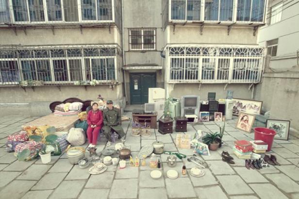 Ein älteres Paar sitzt vor einem Wohnhaus, umgeben von ihrem Hab und Gut.