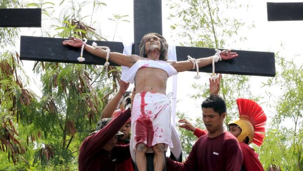 Ein Mann, der Jesus bei einer Kreuzigungszeremonie darstellt, ist an ein Holzkreuz gebunden.