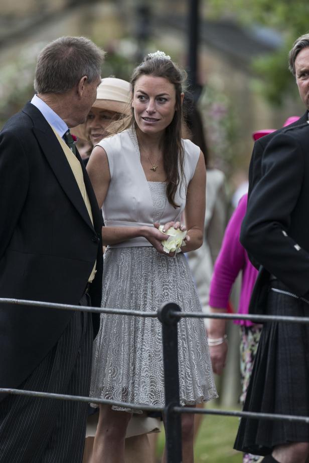 Eine Frau im Kleid hält eine Blume in der Hand, umgeben von anderen Gästen.