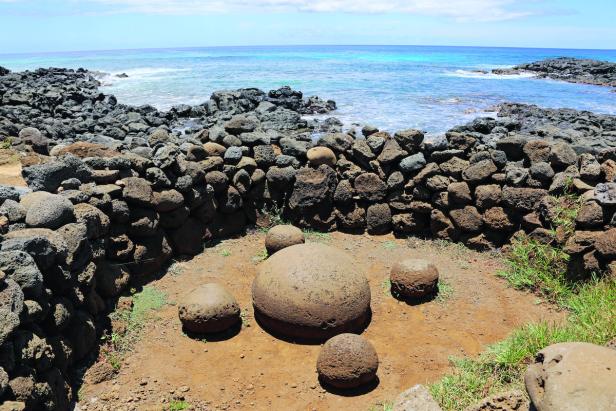 Fünf große Steinkugeln liegen in einem von einer Steinmauer umgebenen Bereich am Meer.