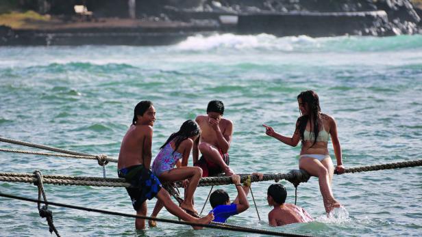 Eine Gruppe von Kindern sitzt und spielt auf einem Seil im Wasser.