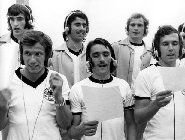 Eine Gruppe deutscher Fußballspieler singt mit Kopfhörern und Notenblättern.