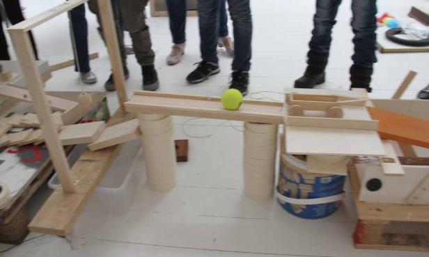 Eine Murmelbahn aus Holz mit einer gelben Kugel und verschiedenen Hindernissen.