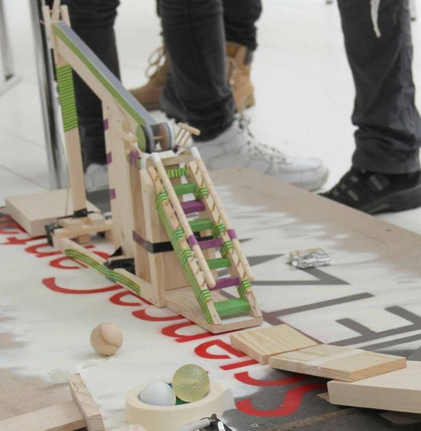 Ein hölzernes Katapult steht auf einem Tisch mit verschiedenen Objekten.