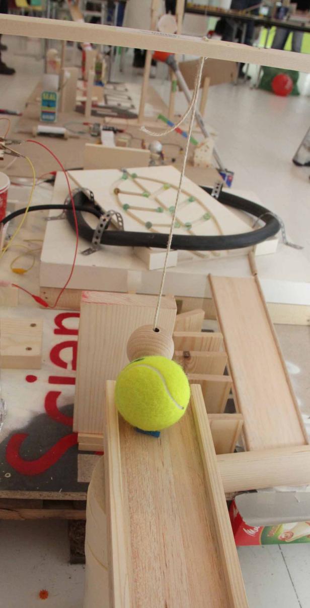 Ein gelber Tennisball liegt auf einer Holzbahn einer Murmelbahn.