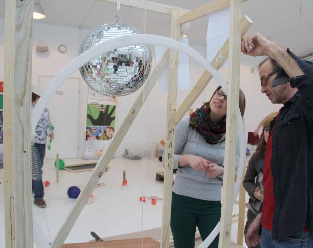 Zwei Personen betrachten eine Installation mit einer Discokugel in einem hellen Raum.