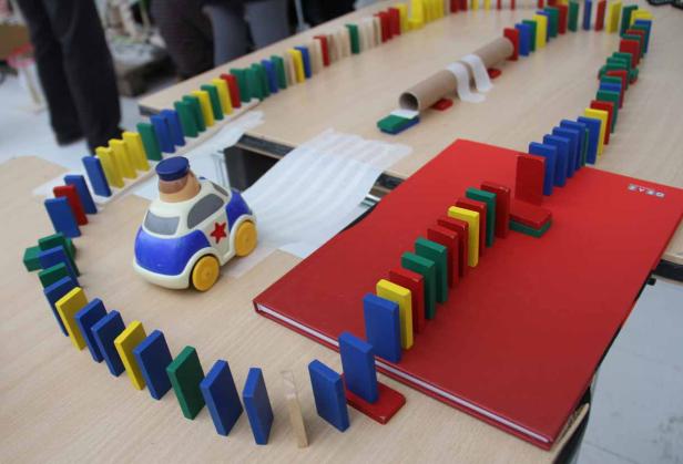 Eine Reihe bunter Dominosteine schlängelt sich um ein Spielzeugauto und einen roten Ordner.