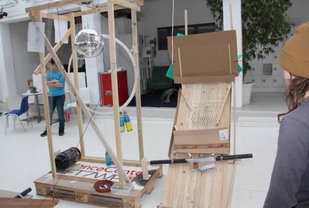 Eine komplexe Installation mit Holzrahmen, Spiegelkugel und verschiedenen Objekten in einem hellen Raum.