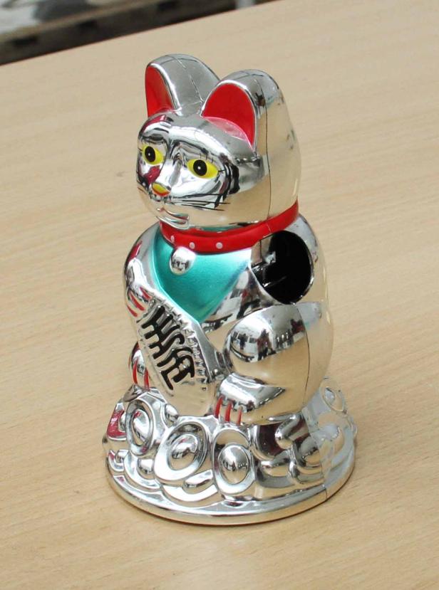 Eine silberne Maneki Neko Winkekatze auf einem Tisch.