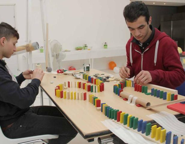 Zwei Jugendliche bauen eine Domino-Kettenreaktion auf einem Tisch.