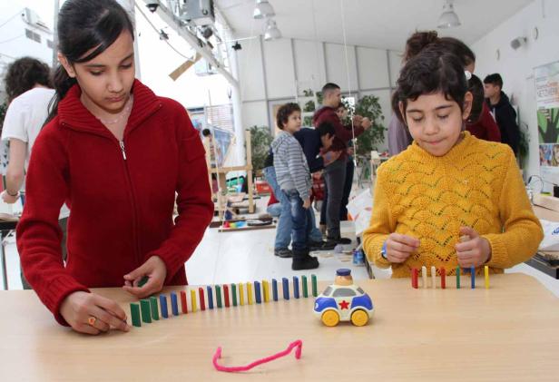 Zwei Mädchen spielen mit Dominosteinen und einem Spielzeugauto.