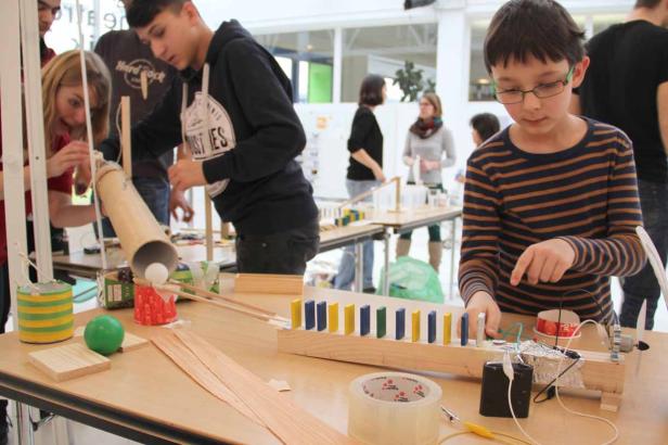 Schüler arbeiten an einer Kettenreaktion mit Dominosteinen und anderen Objekten.