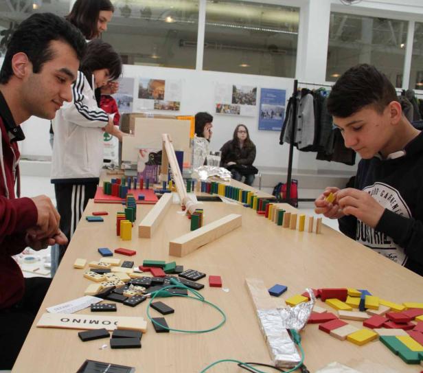Mehrere Personen bauen eine Domino-Kettenreaktion mit bunten Dominosteinen und Holzelementen.