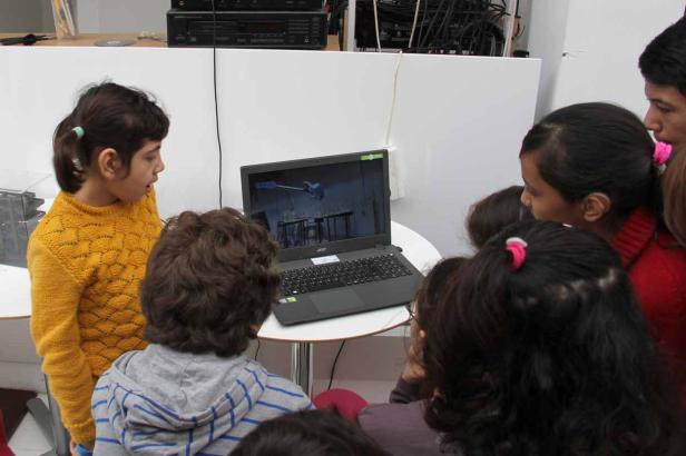 Eine Gruppe Kinder schaut aufmerksam auf einen Laptop auf einem Tisch.