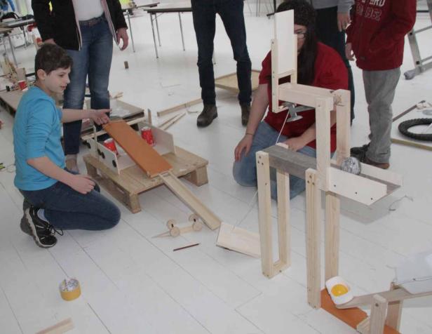 Kinder bauen eine Murmelbahn aus Holz.