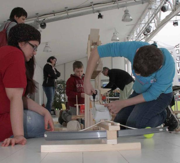 Mehrere Personen bauen gemeinsam an einer Murmelbahn aus Holz.