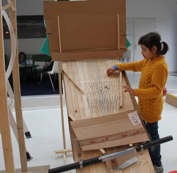 Ein Mädchen spielt mit einer selbstgebauten Murmelbahn aus Holz und Pappe.