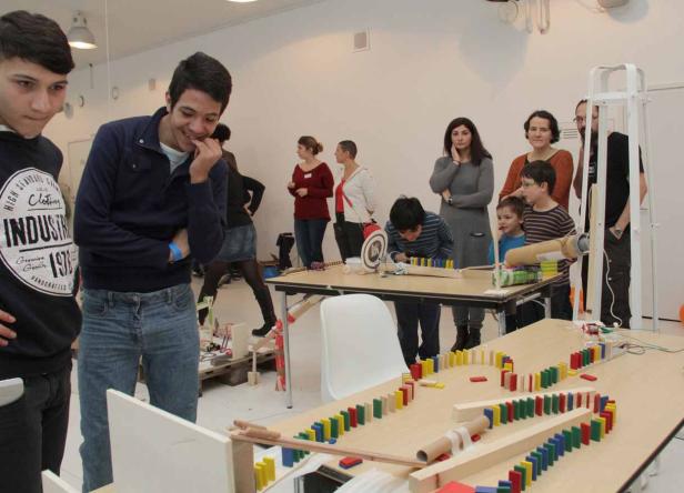 Eine Gruppe von Menschen beobachtet eine Domino-Kettenreaktion auf einem Tisch.