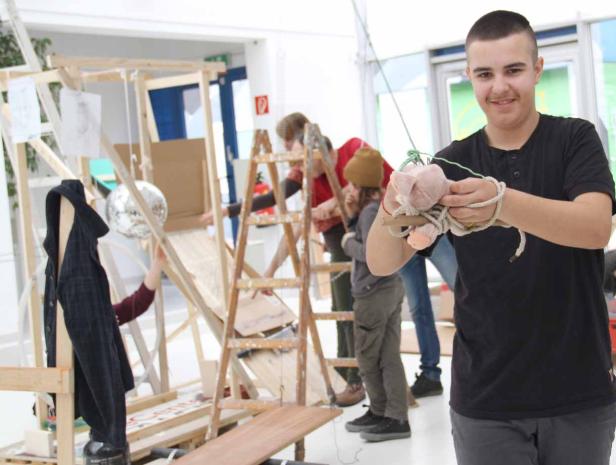 Ein junger Mann hält ein Stofftier, während andere an einer Holzkonstruktion arbeiten.