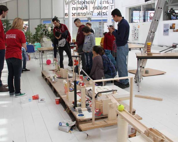 Eine Gruppe von Menschen betrachtet eine komplexe Holzkonstruktion in einem hellen Raum.