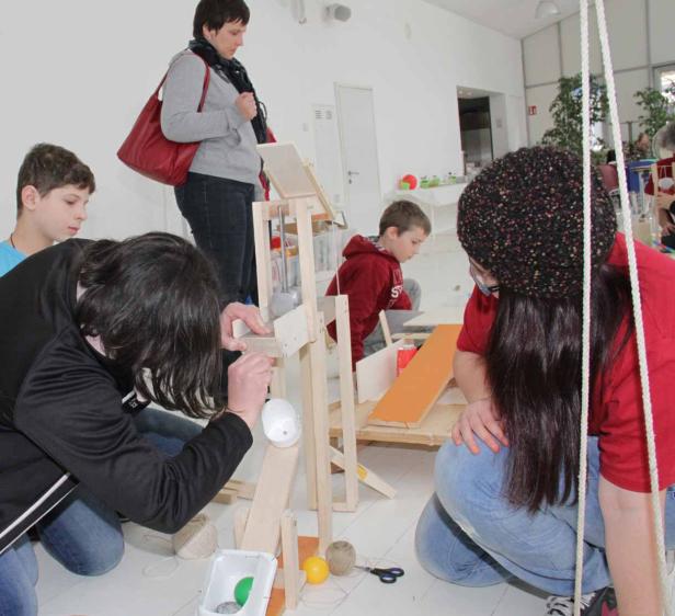 Eine Gruppe von Kindern und Erwachsenen baut gemeinsam an einer Murmelbahn.