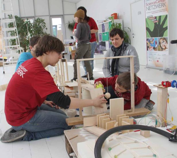 Kinder bauen gemeinsam an einer Murmelbahn aus Holz.