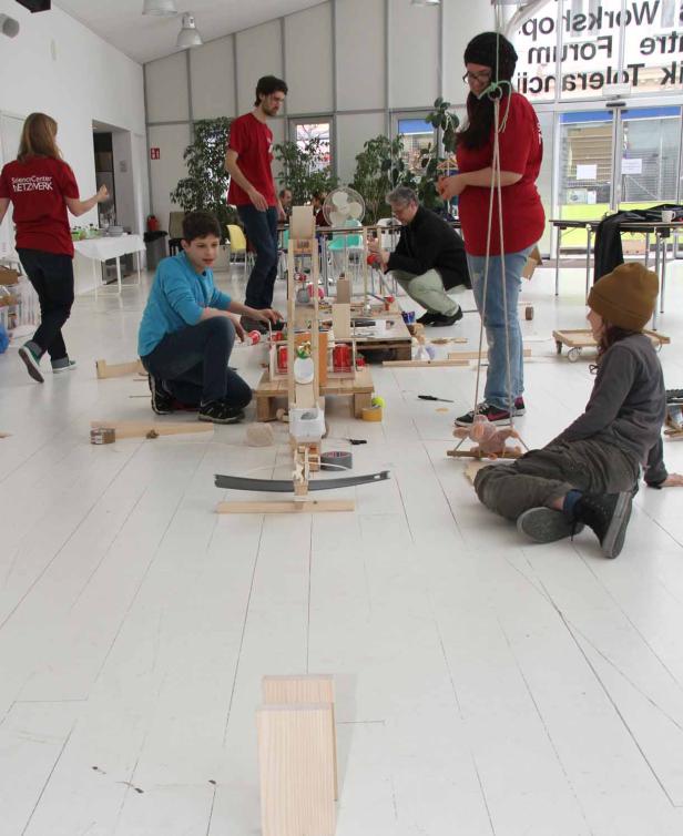 Eine Gruppe von Menschen baut gemeinsam an einer Murmelbahn aus Holz und Alltagsgegenständen.