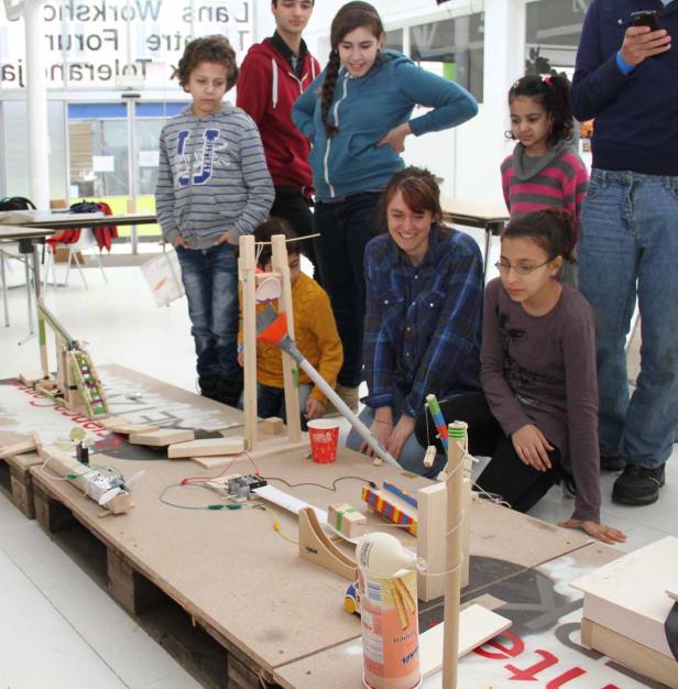 Eine Gruppe von Kindern und eine Frau betrachten eine selbstgebaute Murmelbahn.