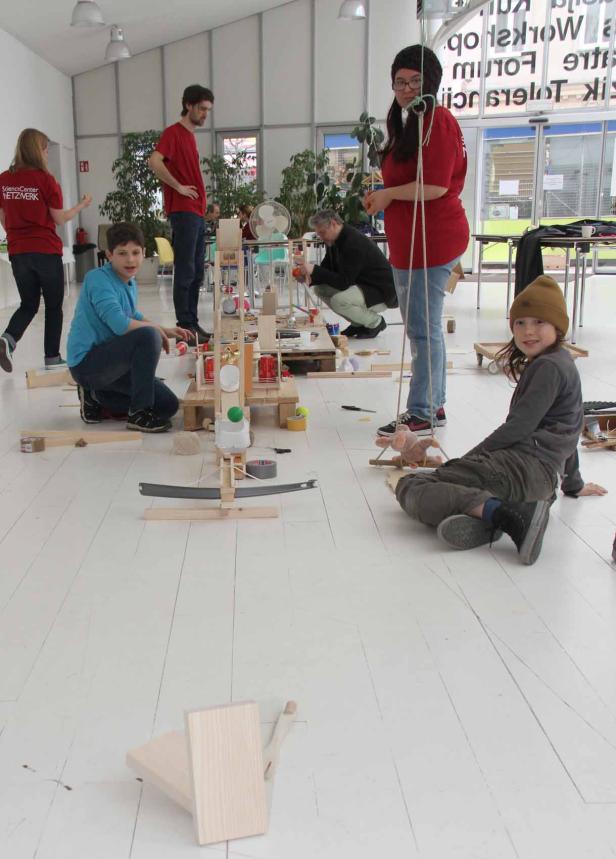 Kinder und Erwachsene bauen gemeinsam an einer Murmelbahn in einem hellen Raum.