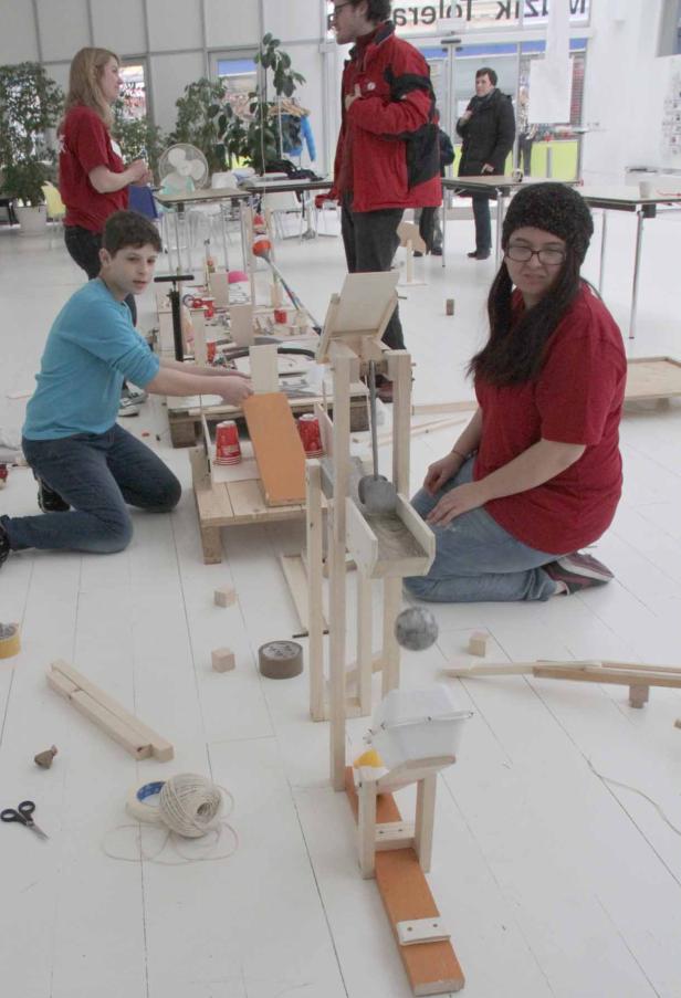 Zwei Personen bauen an einer Murmelbahn aus Holz und anderen Materialien.