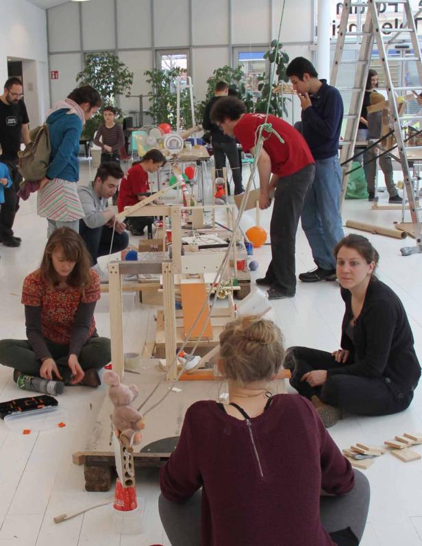 Mehrere Personen bauen gemeinsam an einer komplexen Holzkonstruktion in einem hellen Raum.
