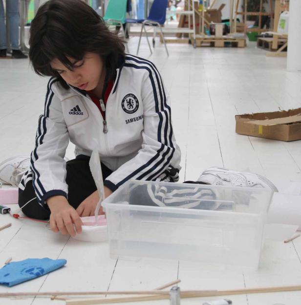 Ein Kind sitzt auf dem Boden und bastelt an einem kleinen Boot.