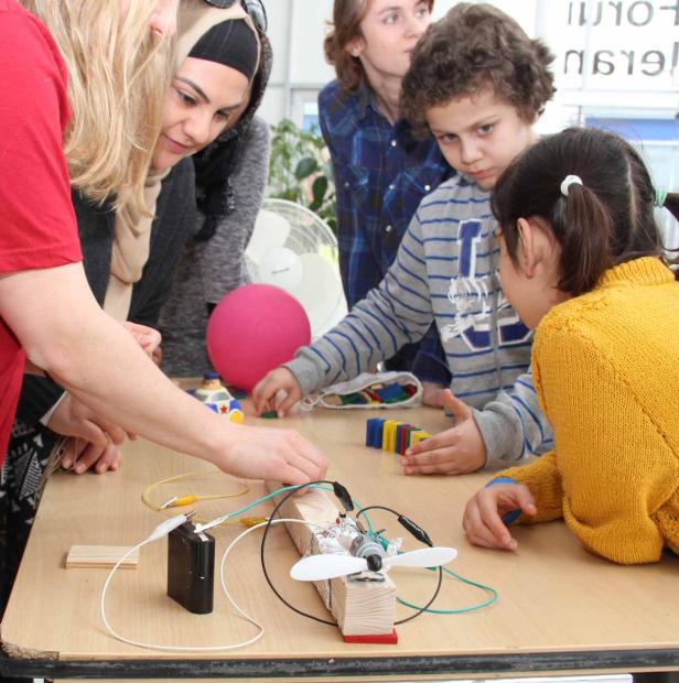 Eine Gruppe von Kindern und Erwachsenen arbeitet an einem kleinen, selbstgebauten Flugzeugmodell.