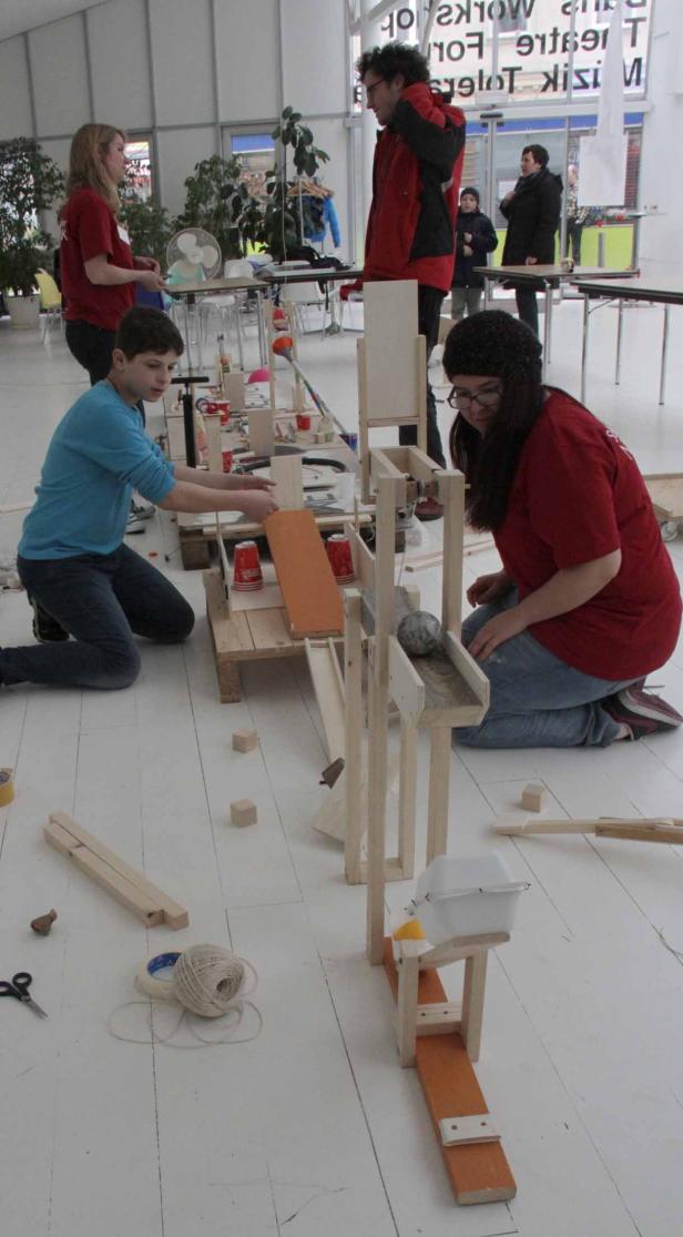 Mehrere Personen bauen gemeinsam an einer Murmelbahn aus Holz.