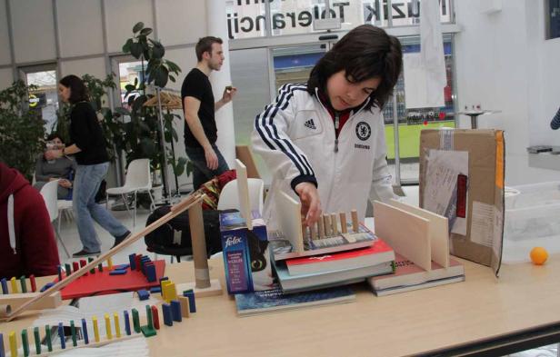 Ein Kind baut eine Murmelbahn mit Dominosteinen und Büchern.