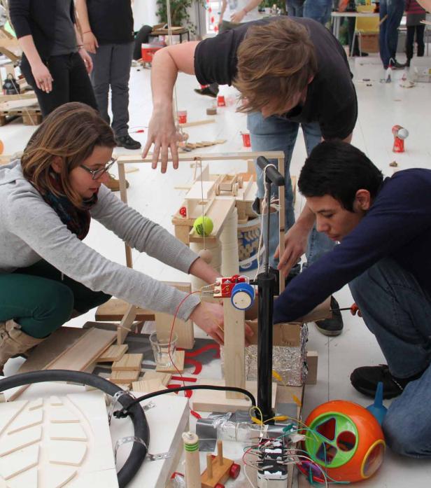 Mehrere Personen arbeiten an einer komplexen Murmelbahn aus Holz und anderen Materialien.