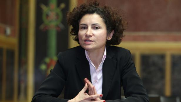 Eine Frau mit lockigem Haar in einem schwarzen Blazer spricht.