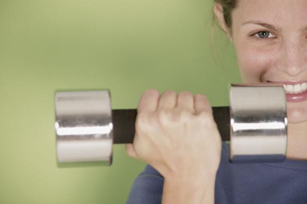 Eine Frau hält eine Hantel vor einem grünen Hintergrund.