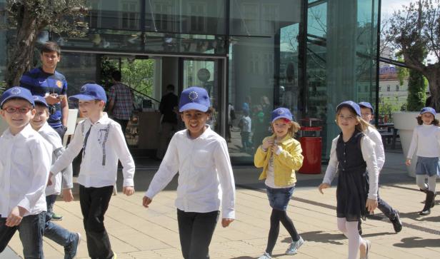 Eine Gruppe von Schulkindern mit EU-Kappen geht auf einem Platz entlang.