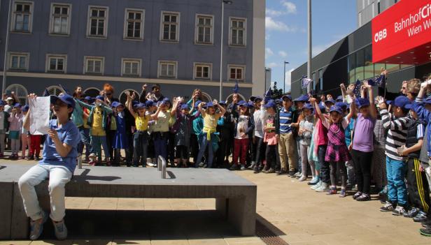 Eine Gruppe Kinder mit EU-Fahnen und -Hüten vor dem Bahnhof Wien West.