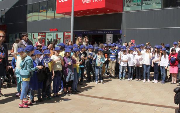 Eine Gruppe Kinder mit EU-Fahnen und blauen Mützen vor dem Wiener Westbahnhof.