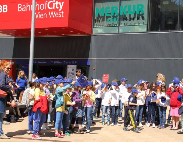 Eine Gruppe Kinder mit EU-Mützen steht vor der BahnhofCity Wien West.