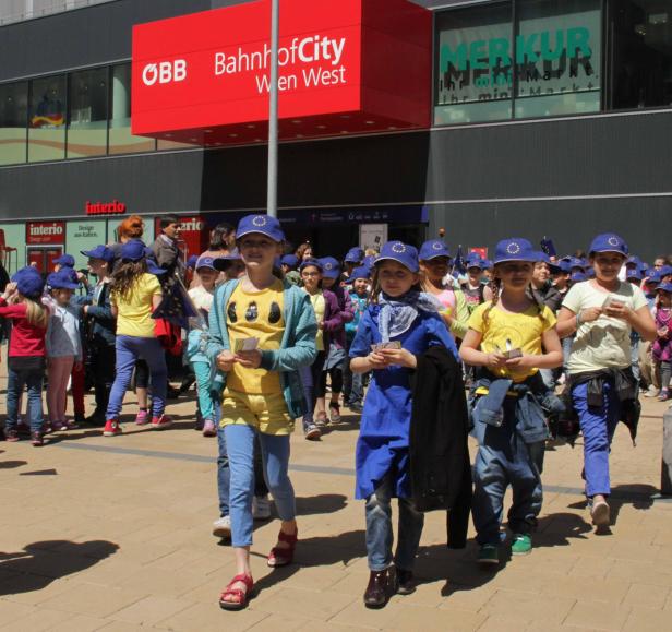 Eine Gruppe von Kindern mit EU-Mützen läuft vor der BahnhofCity Wien West.
