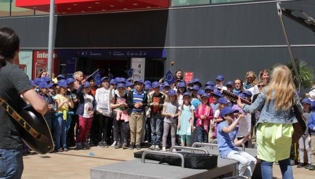 Eine Gruppe Kinder mit EU-Mützen singt vor dem Wiener Westbahnhof.