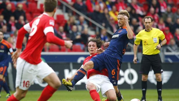 Zwei Fußballspieler kämpfen um den Ball, während ein Schiedsrichter zusieht.